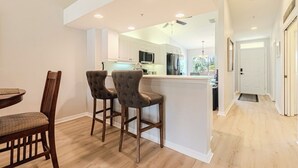 A modern kitchen with white cabinets, a central island, and bar stools. - Relax on the oversized lanai featuring an outdoor kitchen and mid-water view. (Naples)