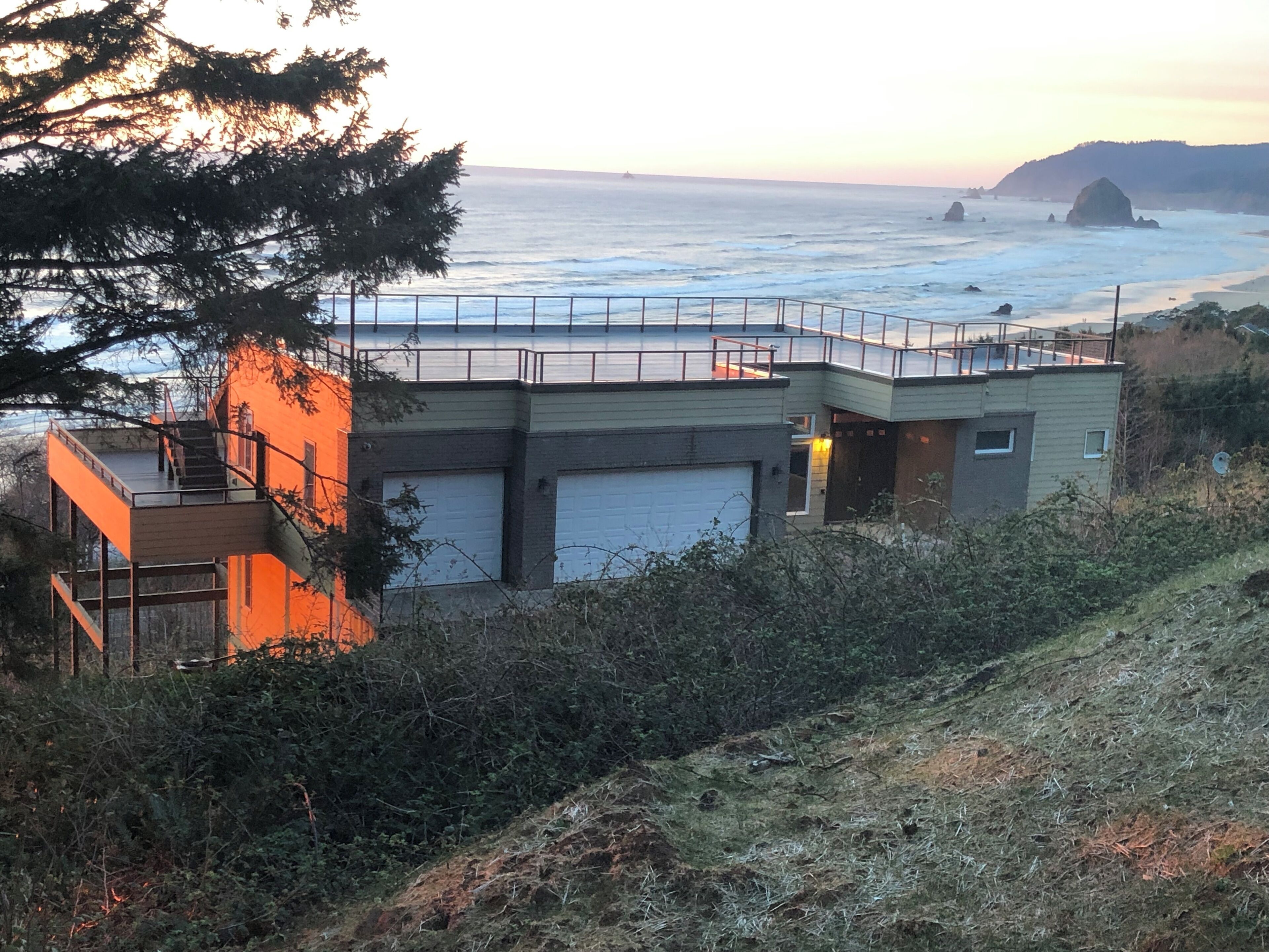 A coastal building with a balcony overlooking the sea, a garage, and a staircase leading to an upper level.