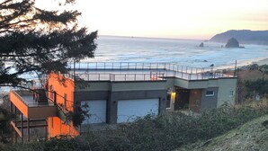 A coastal building with a balcony overlooking the sea, a garage, and a staircase leading to an upper level. - Cannon Beach Arch cape Luxury Vacation Home with Stunning Ocean View (Arch Cape)