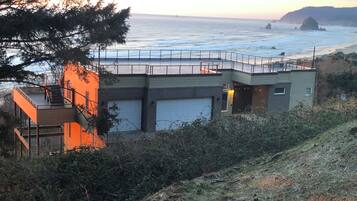 A coastal building with a balcony overlooking the sea, a garage, and a staircase leading to an upper level.