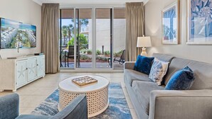 A modern living room with a sofa, coffee table, and TV. There is a sliding glass door leading to a balcony with outdoor furniture.