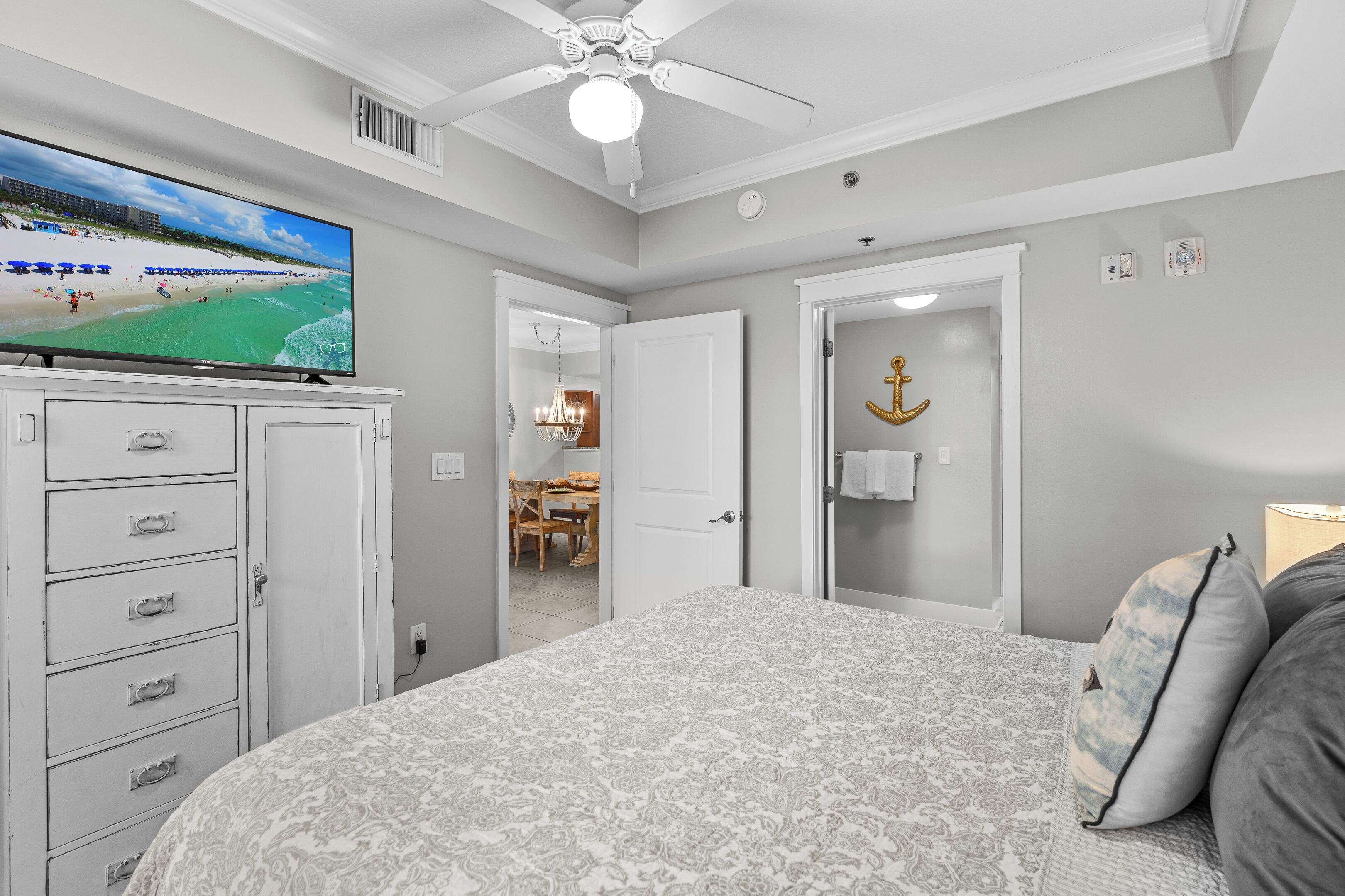 A bedroom with a large bed, a television on a dresser, a ceiling fan, and a door with an anchor decoration.