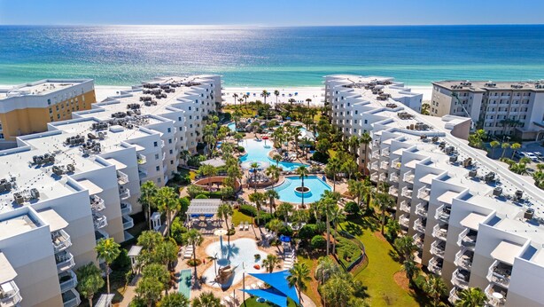 A resort with multiple buildings, a central pool area, and a beach view.