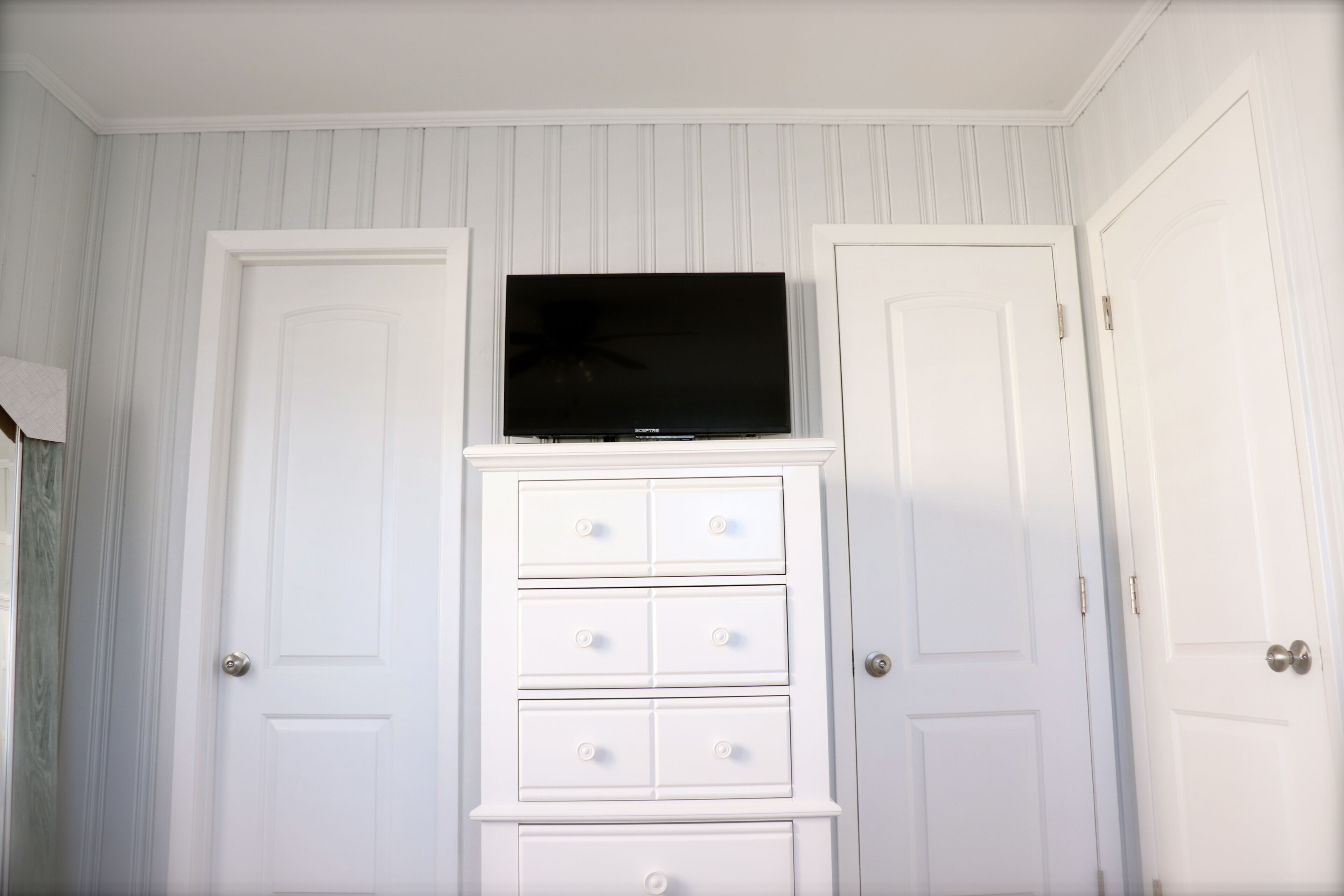 Une pièce avec deux portes blanches, une commode blanche avec des tiroirs et un téléviseur à écran plat posé sur le dessus.
