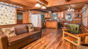 Ein gemütliches Blockhäuschen-Interieur mit Holzboden, Ledersofa, Esstisch und Küchenzeile.