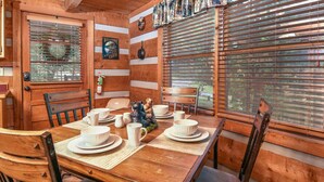 Ein Holzblockhaus-Innenraum mit einem Esstisch, gedeckt für vier Personen, umgeben von Holzstühlen.