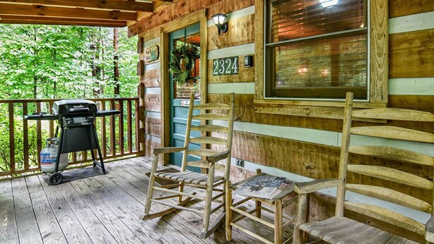 Eine Holzveranda mit Grill, zwei Schaukelstühlen und einer Nummer.'