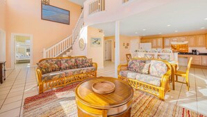 A spacious living room with two floral sofas, a wooden coffee table, and a staircase leading to an upper level. - Oceanside Dog Friendly Home w/ Hot Tub, Game Room, and Beach Nearby (Salvo)