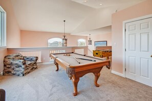 Relax in a spacious room with a pool table, armchair, and foosball table, offering a view of the surrounding landscape.