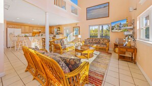 A spacious living area with a high ceiling, a dining area with white chairs, and a kitchen with wooden cabinets. - Oceanside Dog Friendly Home w/ Hot Tub, Game Room, and Beach Nearby (Salvo)