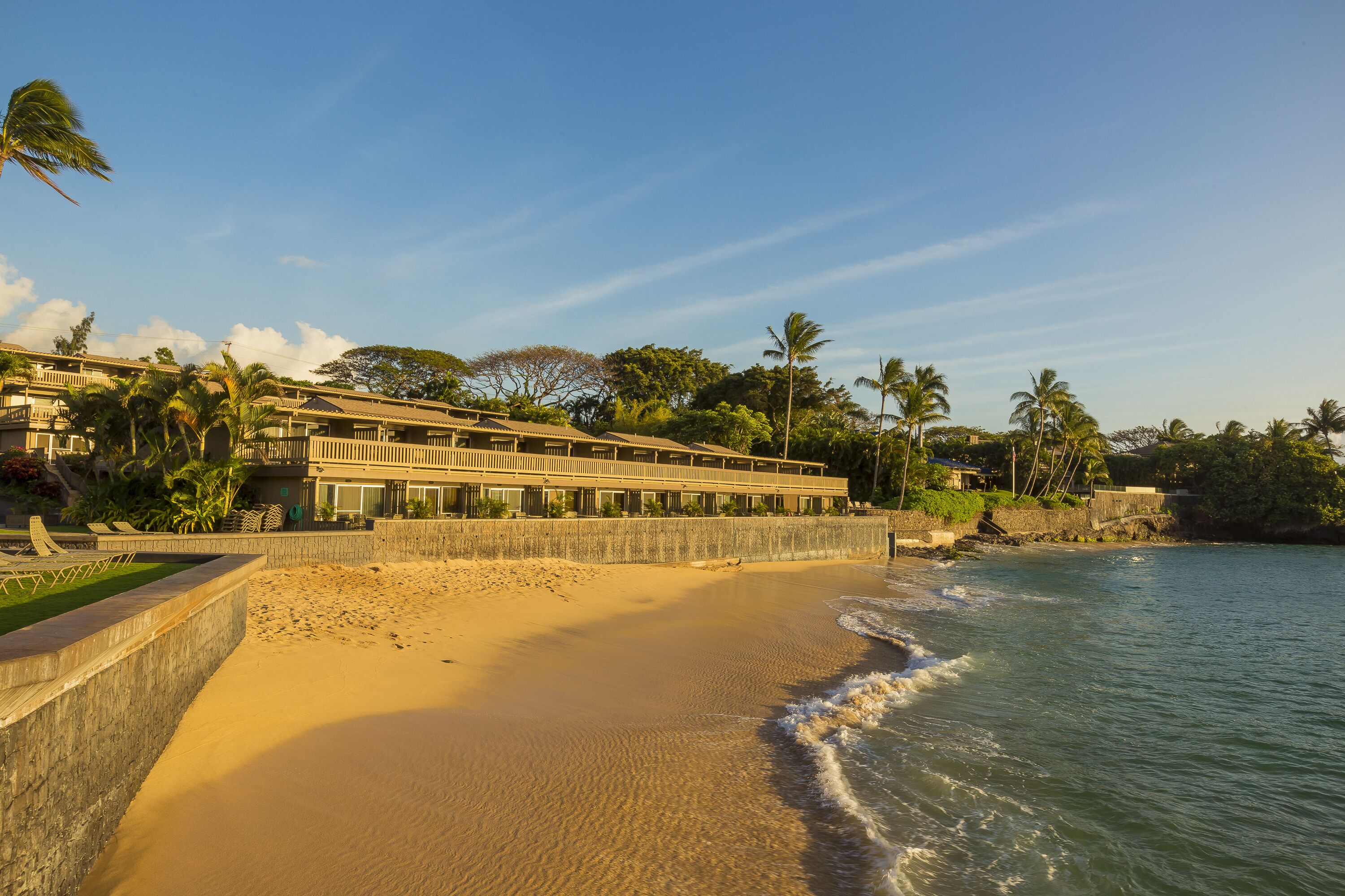Un hotel frente a la playa con un edificio extenso, palmeras y una playa de arena.