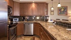Uma cozinha moderna com armários de madeira, eletrodomésticos de aço inoxidável, bancada de granito e backsplash.