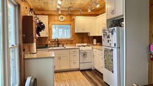 Une cuisine de taille modeste avec des poutres en bois au plafond, des armoires blanches, une cuisinière à gaz et un réfrigérateur.