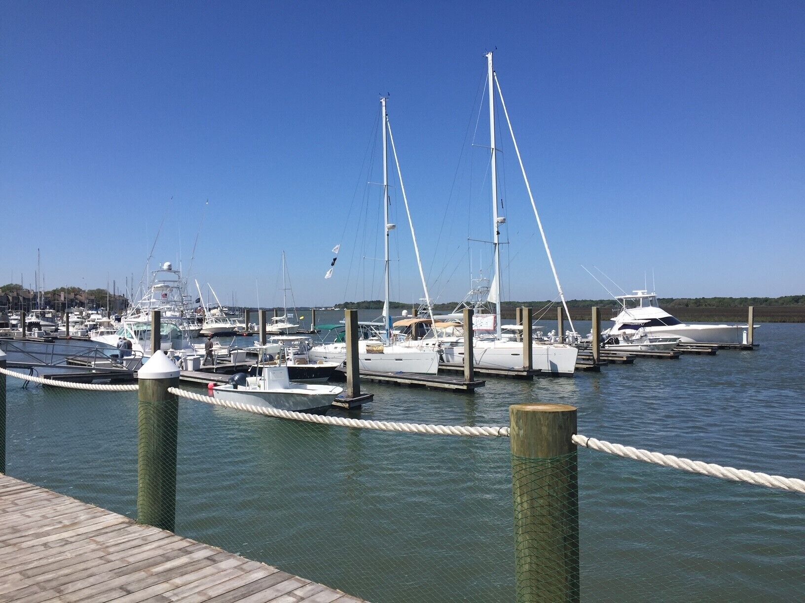 Un port de plaisance où sont amarrés différents types de bateaux, avec des pilotis en bois et un ciel d’un bleu limpide.