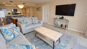 A living room with a sofa, coffee table, and TV. There is a kitchen in the background. - Experience comfort in this 2-bedroom condo with a bonus room, perfect for 8 guests. (South Padre Island)