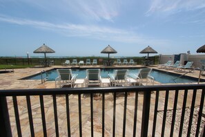 Un área de piscina con sillones de descanso y sombrillas, cielo despejado y vista al océano.