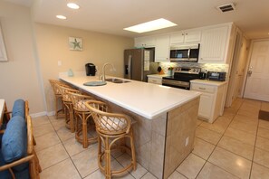 A kitchen with a central island, bar stools, a refrigerator, a microwave, and a stove. - Experience comfort in this 2-bedroom condo with a bonus room, perfect for 8 guests. (South Padre Island)