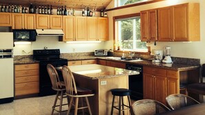 Une cuisine spacieuse avec des meubles en bois, un grand îlot central doté de tabourets, un four encastré et un ventilateur de plafond.