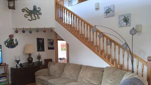 Un salon avec un escalier en bois, un canapé beige, une table basse en verre et divers éléments de décoration murale, notamment un tableau représentant un hippocampe et une tortue.