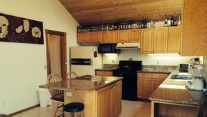 Une cuisine avec des meubles en bois, un plan de travail en granit, une cuisinière noire, un four à micro-ondes et un réfrigérateur.