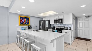 Una cocina moderna con armarios blancos, una isla grande con taburetes de bar, un refrigerador, microondas, tostadora y cafetera.
