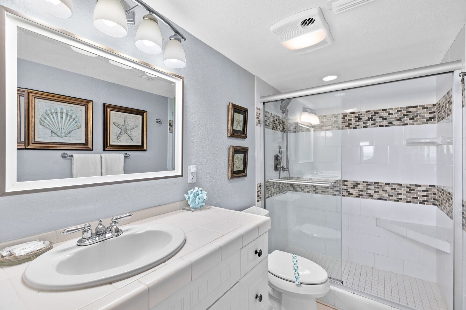 A bathroom with a white sink, a toilet, a glass shower enclosure, and framed artwork on the wall.