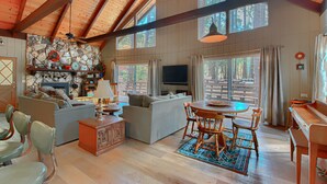 A spacious living area with a wooden ceiling, a stone fireplace, a sofa, a television, and a dining table with chairs.