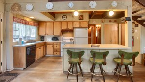 A kitchen with wooden cabinets, a central island with bar stools, a microwave, a refrigerator, and a clock on the wall.