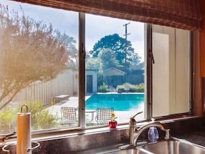 Une cuisine dotée d’une grande fenêtre donnant sur un jardin avec une piscine.