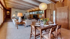 Amplia sala de estar con techo de madera, una mesa de comedor preparada para cuatro personas y un rincón de descanso acogedor.