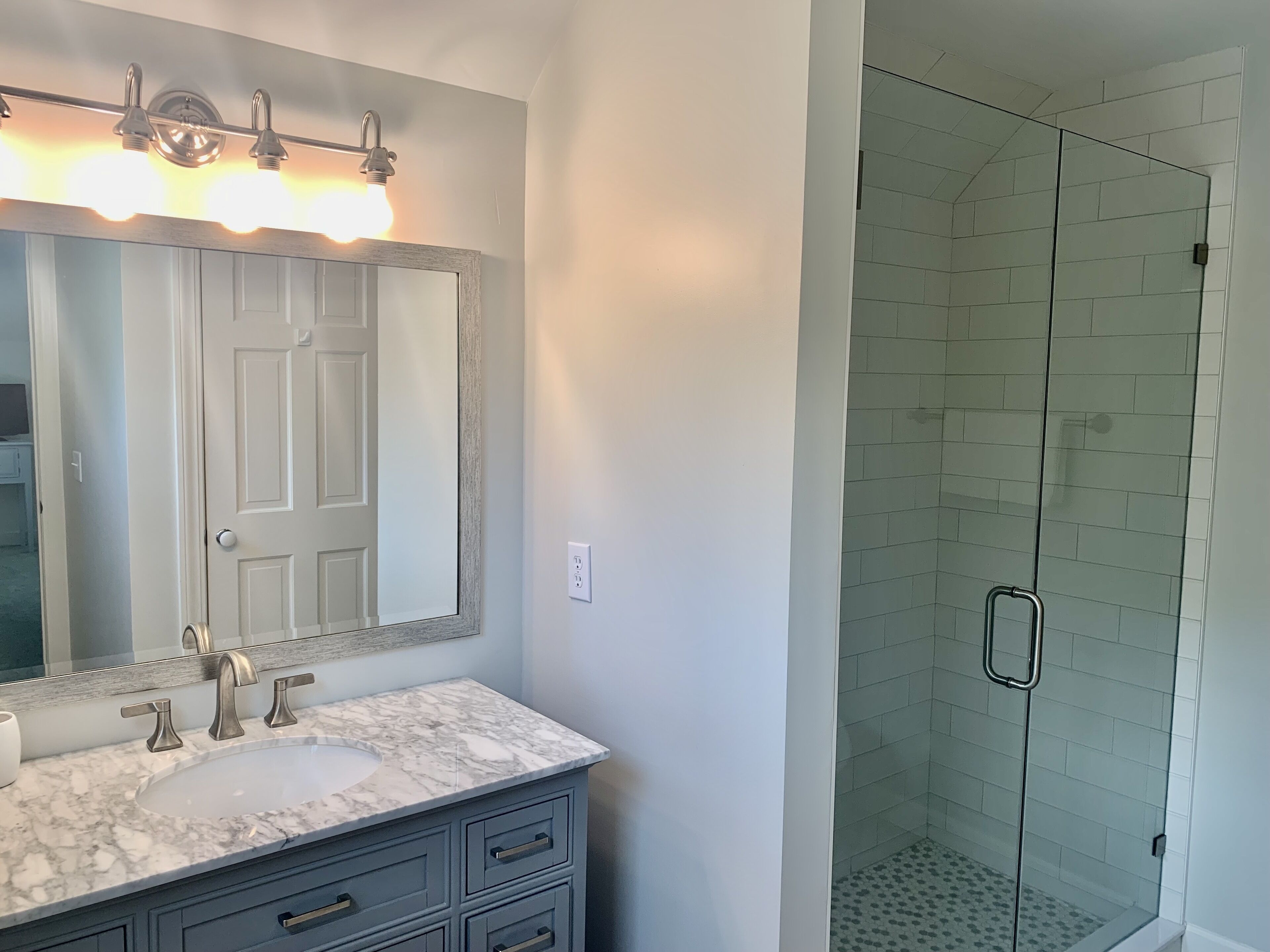 Une salle de bain avec un lavabo blanc, un grand miroir et une douche à parois de verre.