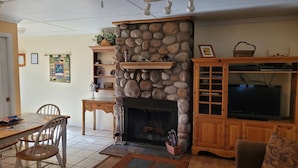 A living room with a stone fireplace, wooden furniture, a television, and a fireplace screen. - COMY, COZY COTTAGE! HOT TUB ! PETS BY APPROVAL 
BEAUTIFUL IN THE FALL! BOOK NOW (Ruidoso)