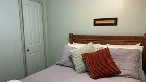 A bedroom with a bed, pillows, a wooden headboard, a door, and a wall-mounted sign. - COMY, COZY COTTAGE! HOT TUB ! PETS BY APPROVAL 
BEAUTIFUL IN THE FALL! BOOK NOW (Ruidoso)