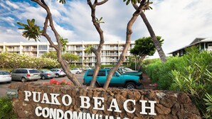 Schild für die Puako Beach Condominiums, mit einem Parkplatz und einem Gebäude im Hintergrund.