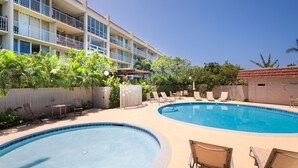 Ein Hotel mit zwei Schwimmbecken, Liegestühlen und einem gepflegten Garten.