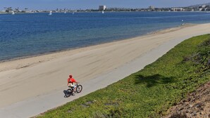 A coastal road with a cyclist, a sandy beach, and a body of water with sailboats. - Crown Point Beach House - Beach and Water on 3 Sides! (San Diego)