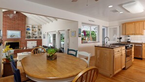 A spacious kitchen with wooden cabinets, a central island, and a dining area with a round table and chairs. - Crown Point Beach House - Beach and Water on 3 Sides! (San Diego)
