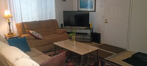 A living room with a sofa, a coffee table, a television, and a door.