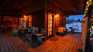 A wooden cabin with a porch, furnished with a sofa, chairs, and a table.