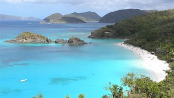A coastal landscape with a beach, clear turquoise waters, and lush greenery.