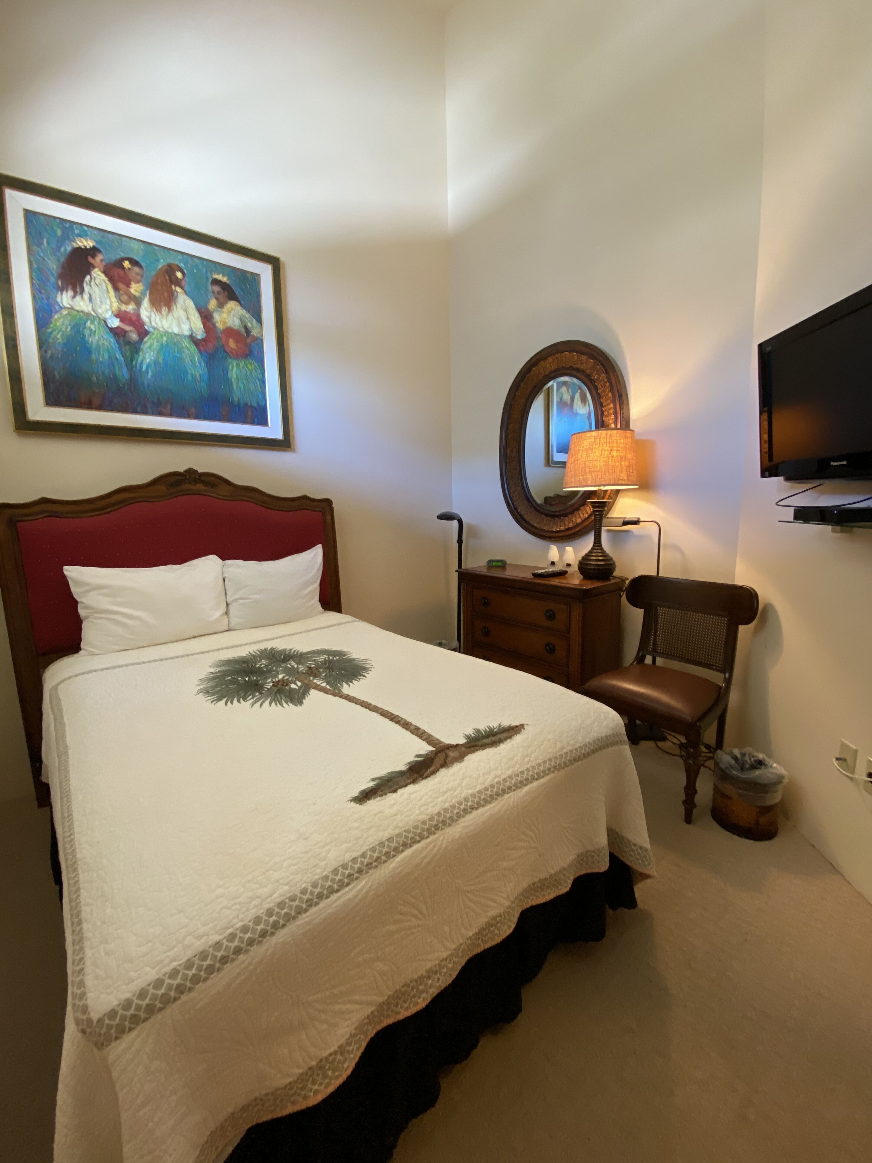A hotel room with a bed, a nightstand, a chair, a TV, and a painting on the wall.