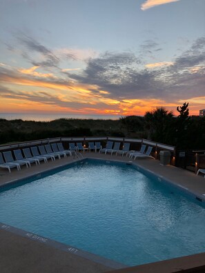 Una piscina con sillas de descanso y vistas al atardecer.