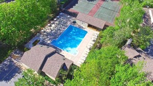 Vista aérea de una zona residencial con piscina, canchas de tenis y un área de patio cubierta.
