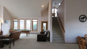 Un salon spacieux avec une table de billard, une cheminée et une vue sur l’extérieur grâce à de grandes fenêtres.