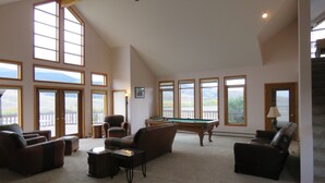 Un salon spacieux avec une table de billard, des sièges confortables, de grandes fenêtres et une vue sur l’extérieur.