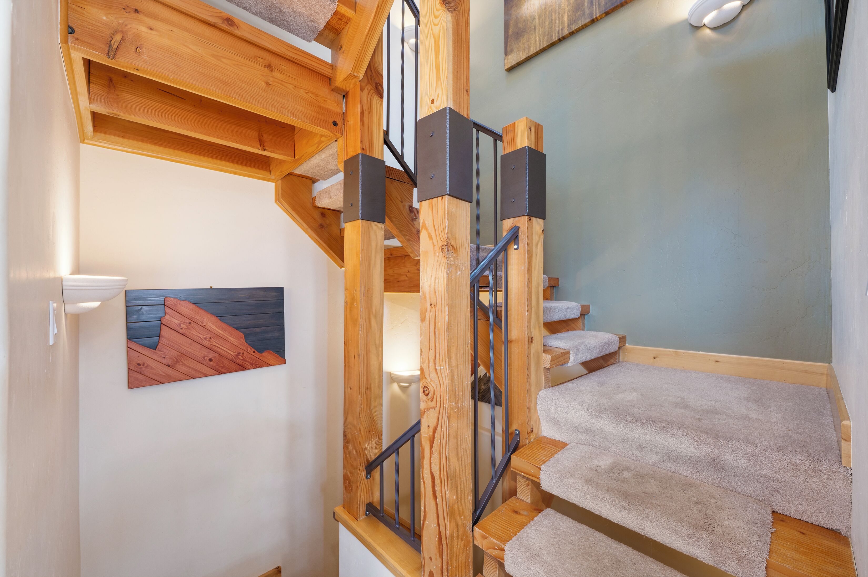 Un escalier en bois avec une rampe, des marches recouvertes de moquette et un luminaire fixé au mur.