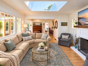 A spacious living room with a large sectional sofa, a round coffee table, and a fireplace. - Hammonds Beach Haven - next to Miramar Beach w/ yard, deck & sunroom - walk to Rosewood! (Santa Barbara)