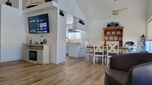A spacious living area with a fireplace, a TV mounted on the wall, and a dining area with chairs and a table.
