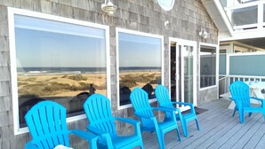 A deck with blue Adirondack chairs and large windows overlooking a beach.
