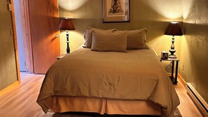 A bedroom with a large bed, two bedside lamps, a framed picture on the wall, and a wooden door.